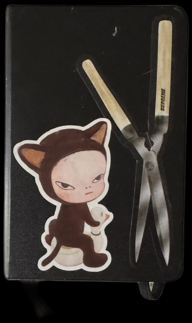 black sketchbook with a cat character and scissors sticker
